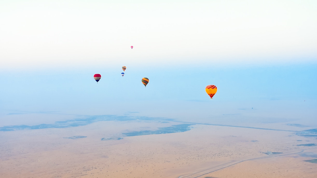 Hot air balloon over Dubai desert at sunrise with falcon and camel ride experience.