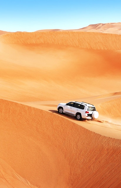 SUV driving over sand dunes in Dubai desert safari.