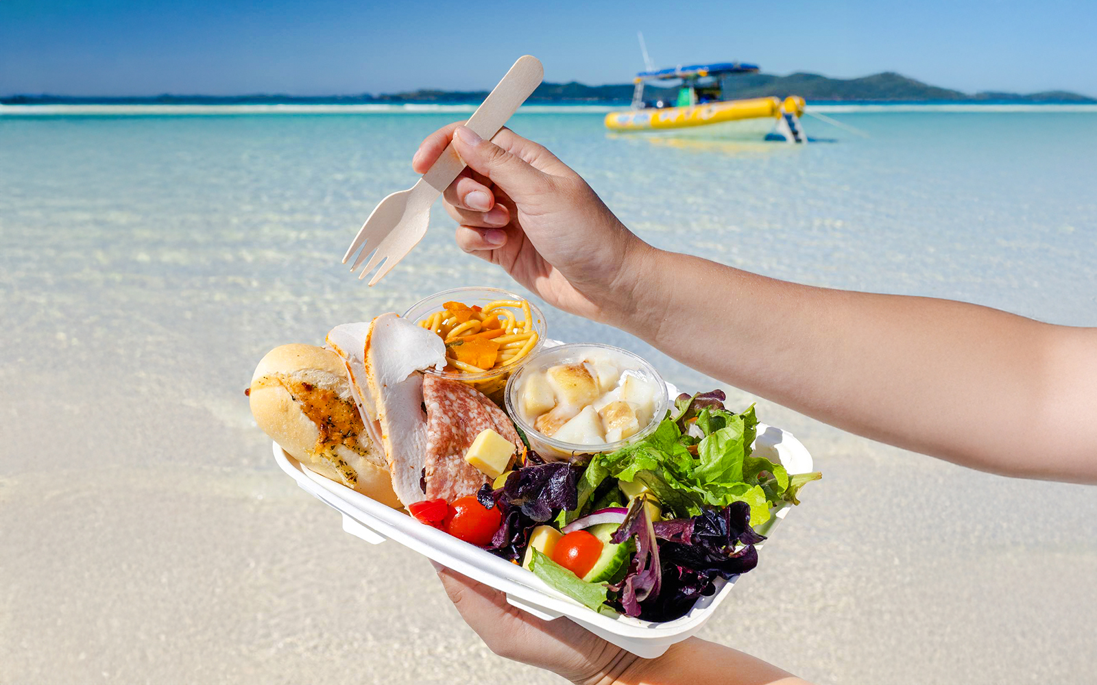 Lunch served on Whitsundays beach with a boat in the background.