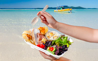 Lunch served on Whitsundays beach with a boat in the background.