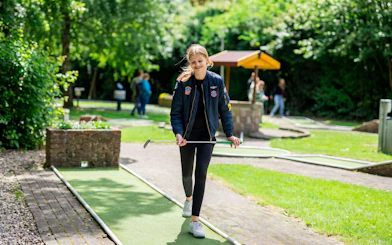 Young person playing mini golf at Midgetgolf Parkhaven, surrounded by greenery.