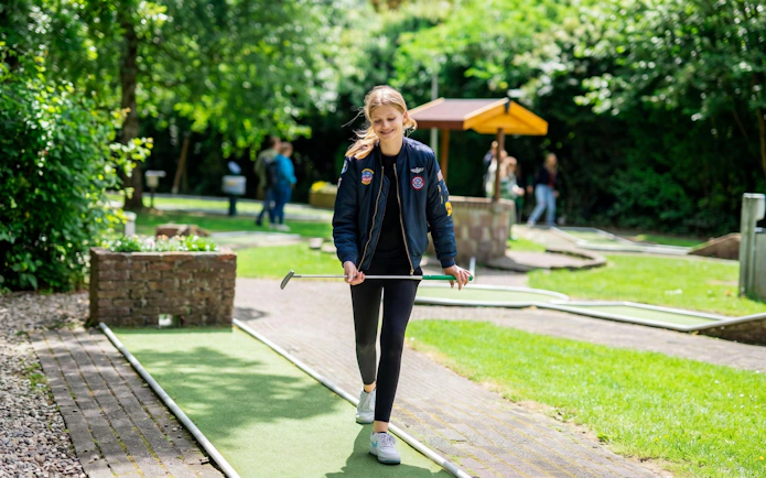 Young person playing mini golf at Midgetgolf Parkhaven, surrounded by greenery.