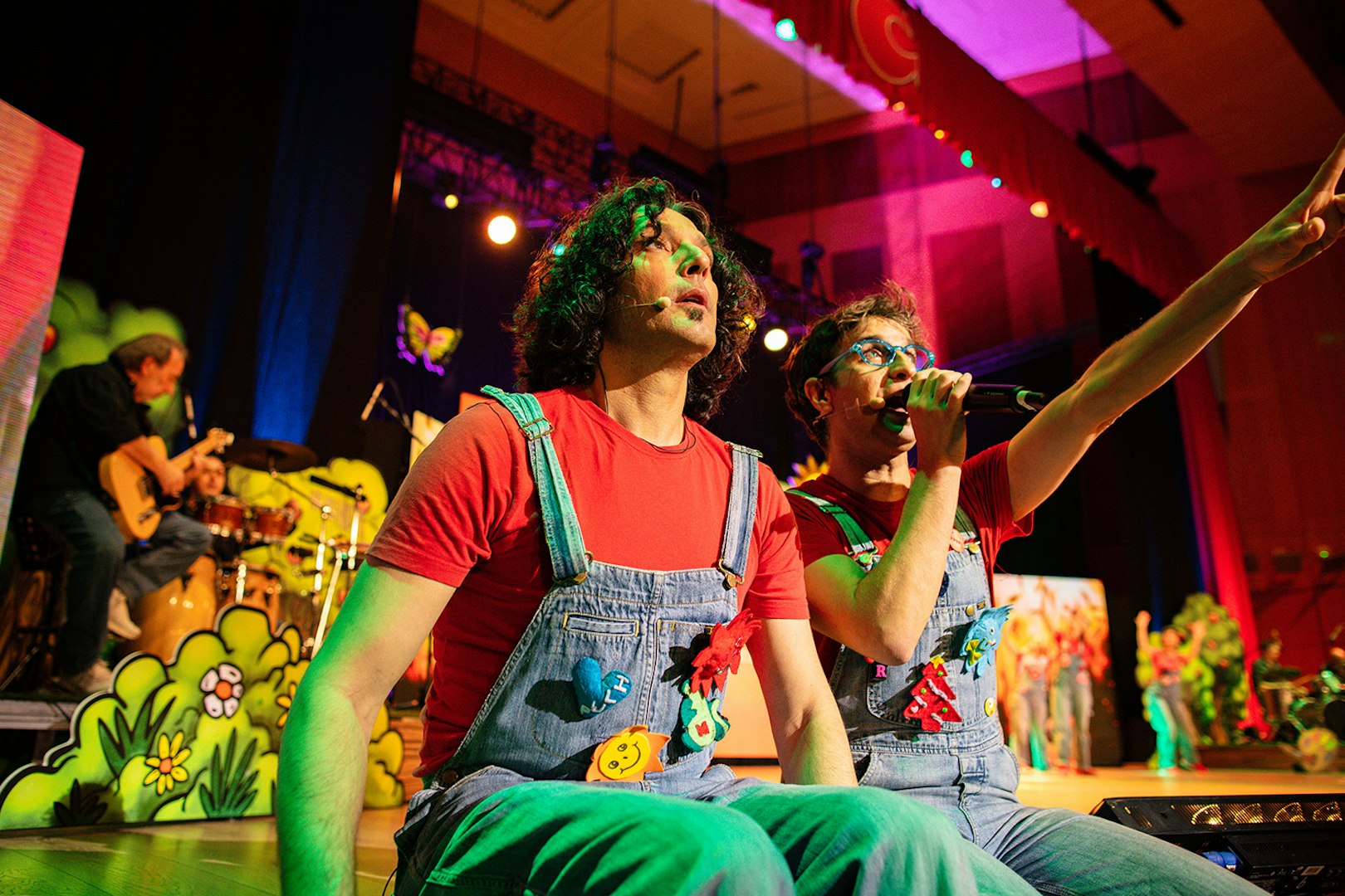 Performers on stage during Cantajuegos 20 Años concert, with colorful backdrop and musicians.