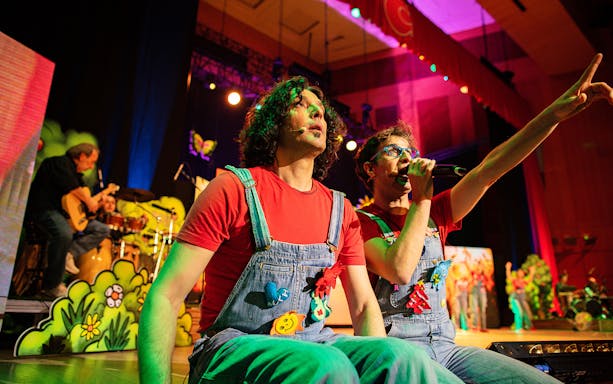 Performers on stage during Cantajuegos 20 Años concert, with colorful backdrop and musicians.