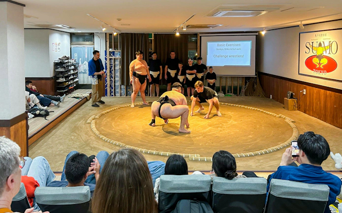 Sumo demonstration in Tokyo with a former wrestler guiding participants in a practice ring.