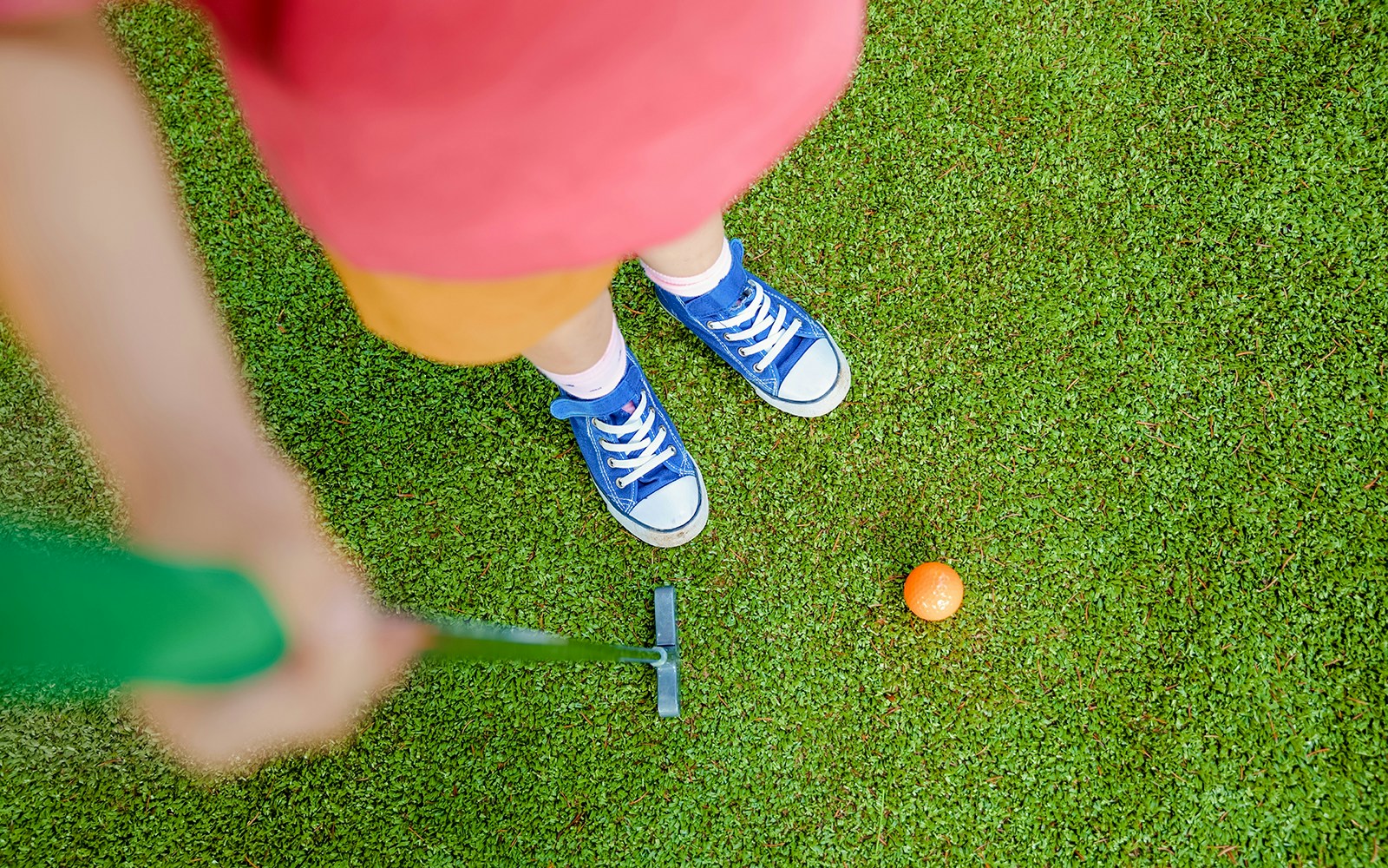 Girl aiming to putt orange ball on mini golf course.