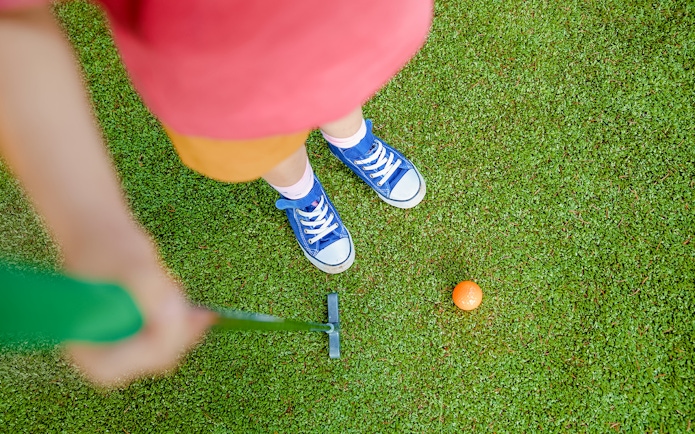 Girl aiming to putt orange ball on mini golf course.