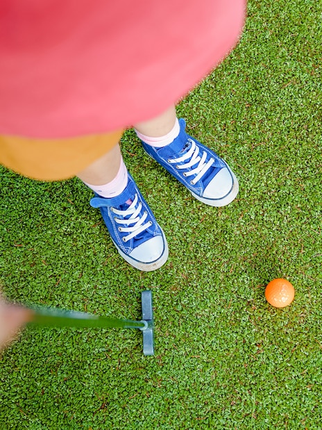 Girl aiming to putt orange ball on mini golf course.