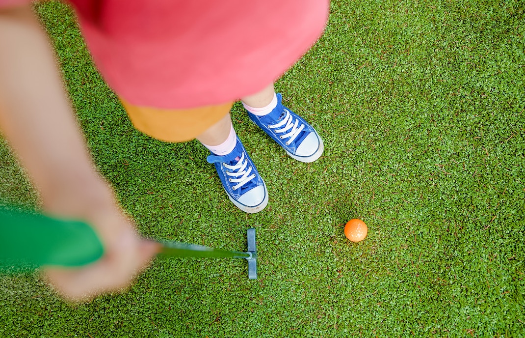 Girl aiming to putt orange ball on mini golf course.