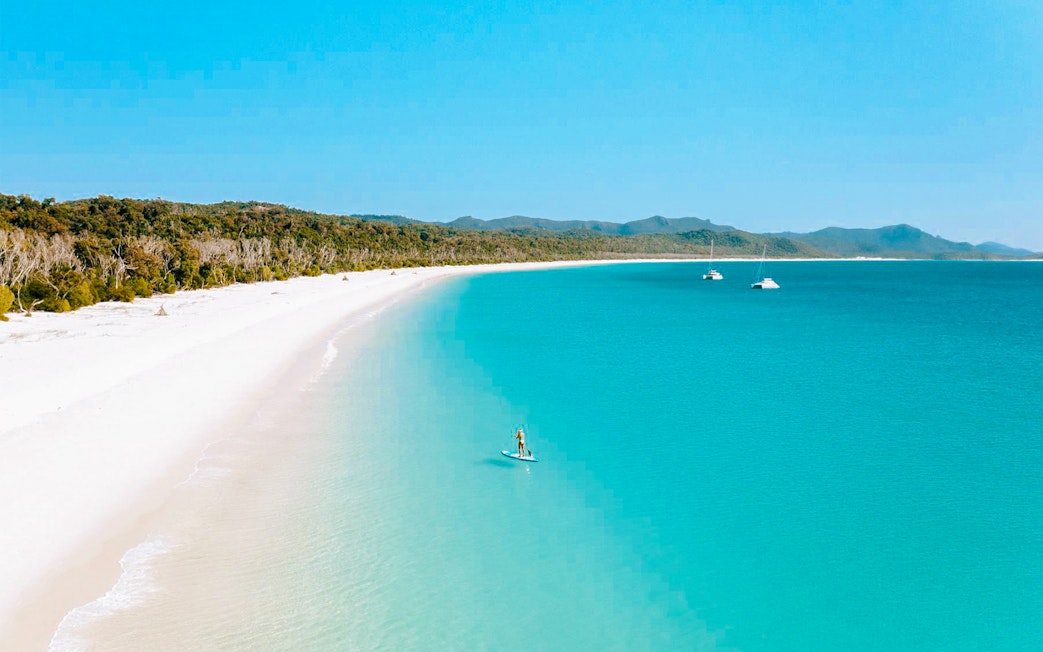 Paddleboarder on turquoise waters near Whitsundays Islands beach.