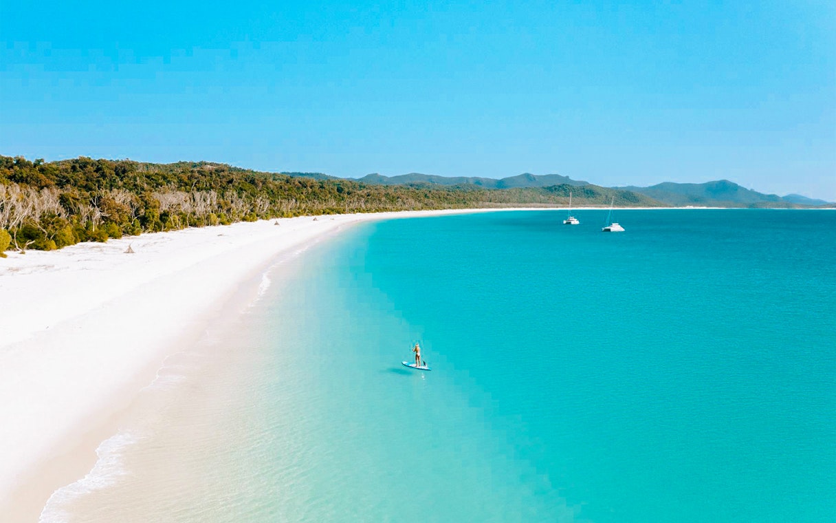 Paddleboarder on turquoise waters near Whitsundays Islands beach.