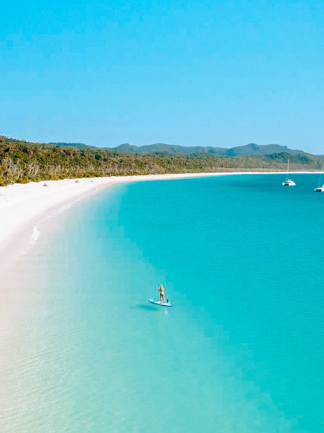 Paddleboarder on turquoise waters near Whitsundays Islands beach.