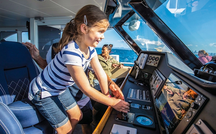 Child interacting with navigation console in boat's pilot room.
