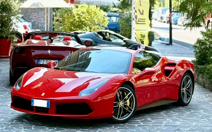 Red Ferrari 488 parked on a cobblestone street with greenery in the background.