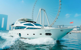 Luxury yacht cruising near Dubai Harbour with Ferris wheel in the background.