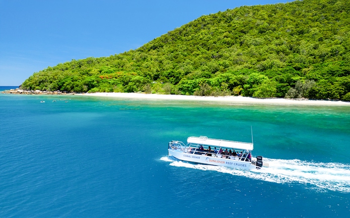 Glass bottom boat near Fitzroy Island, Australia, with lush greenery and clear blue water.