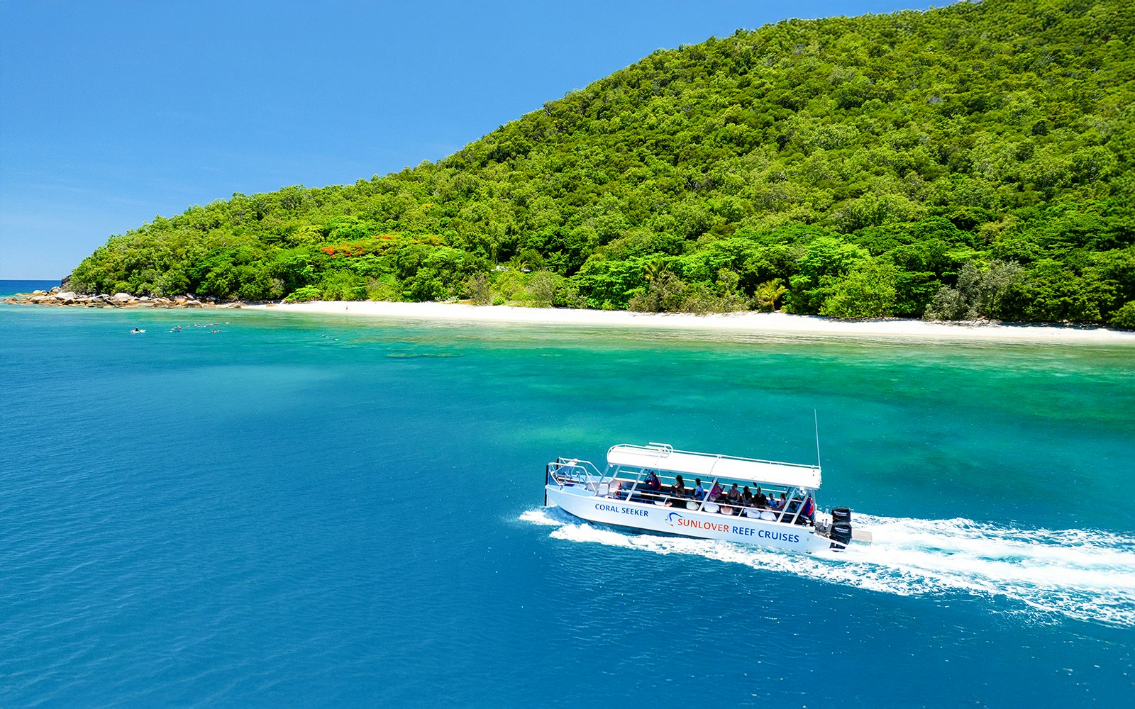 Glass bottom boat near Fitzroy Island, Australia, with lush greenery and clear blue water.