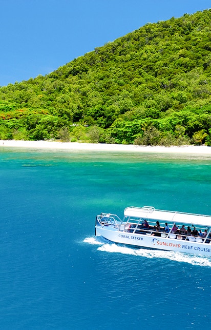 Glass bottom boat near Fitzroy Island, Australia, with lush greenery and clear blue water.