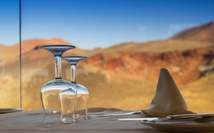 Wine glasses and napkin on a table with Timanfaya National Park landscape in the background.