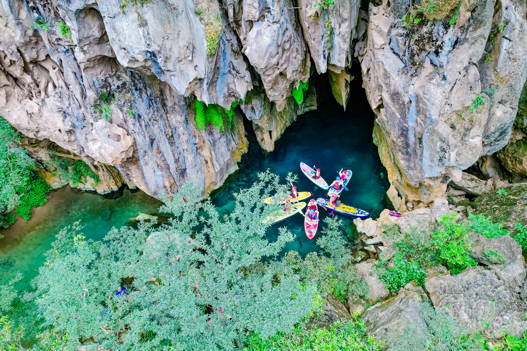 Kayakers exploring E Cave entrance in lush Abandoned Valley, Phong Nha, Vietnam.