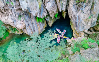 Kayakers exploring E Cave entrance in lush Abandoned Valley, Phong Nha, Vietnam.