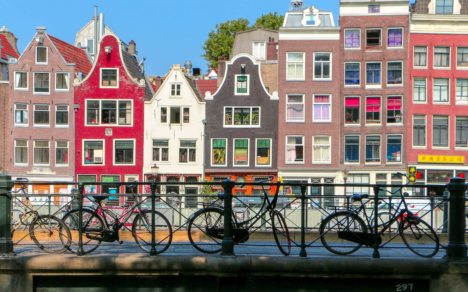 Bicycles on a canal bridge with colorful gabled houses in Amsterdam.