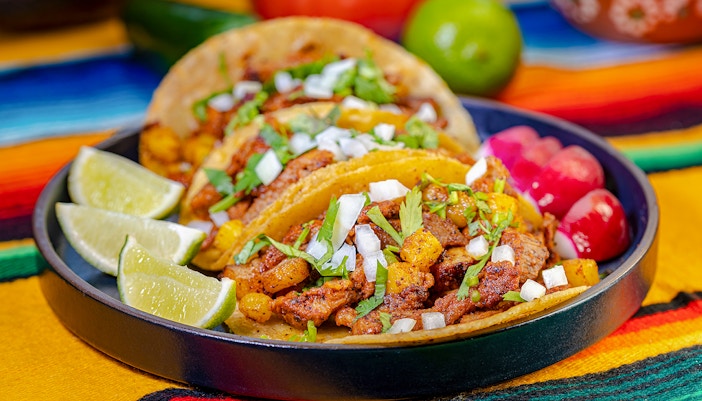Al Pastor tacos with pineapple, onions, and cilantro on a colorful tablecloth.