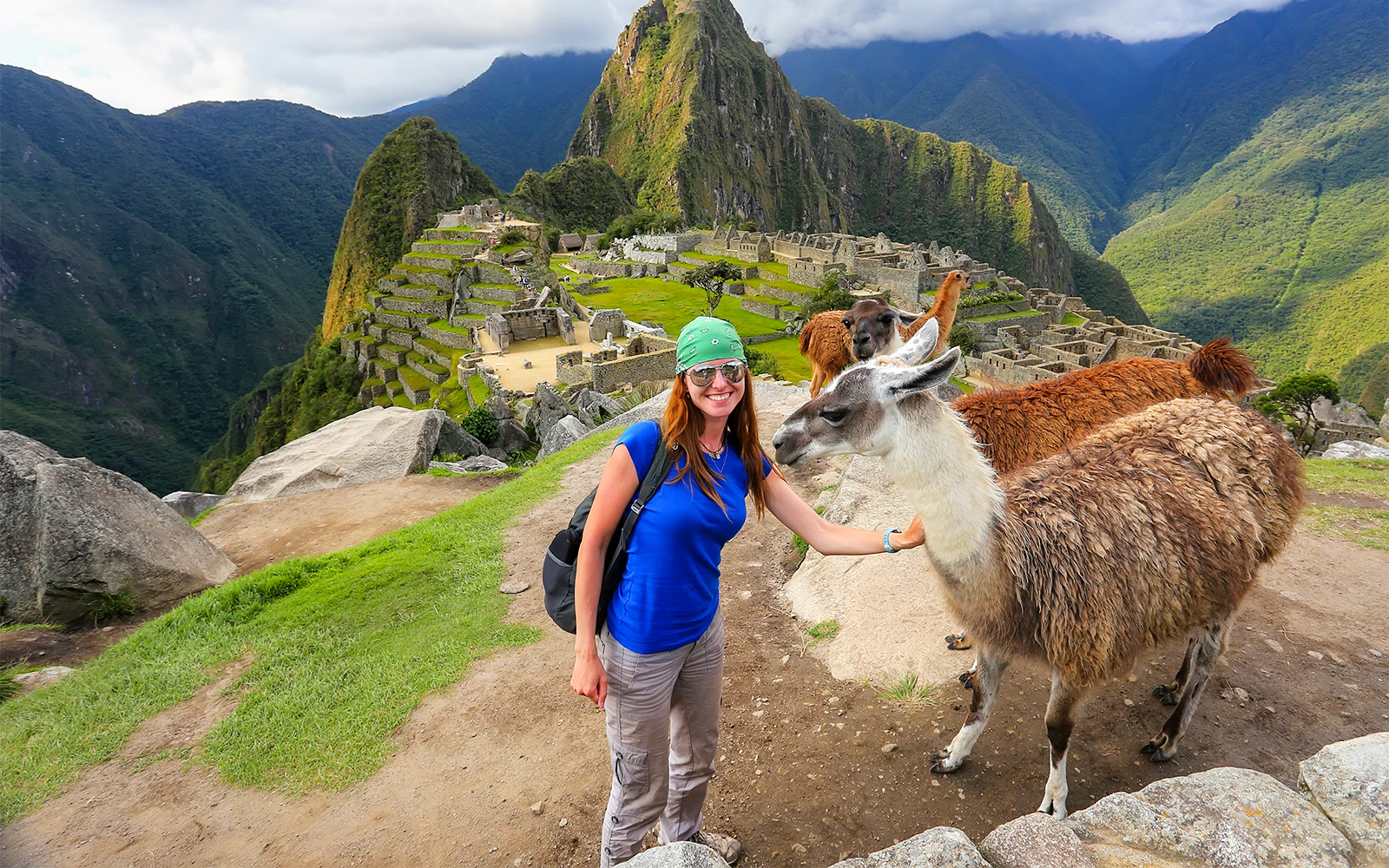 Traveler with llamas at Machu Picchu, Peru, with ancient ruins and mountains in the background.