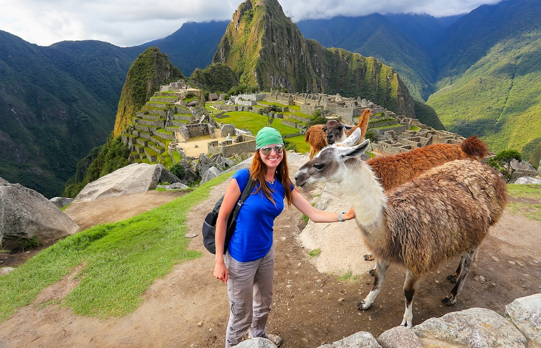 Traveler with llamas at Machu Picchu, Peru, with ancient ruins and mountains in the background.
