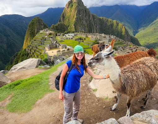 Traveler with llamas at Machu Picchu, Peru, with ancient ruins and mountains in the background.
