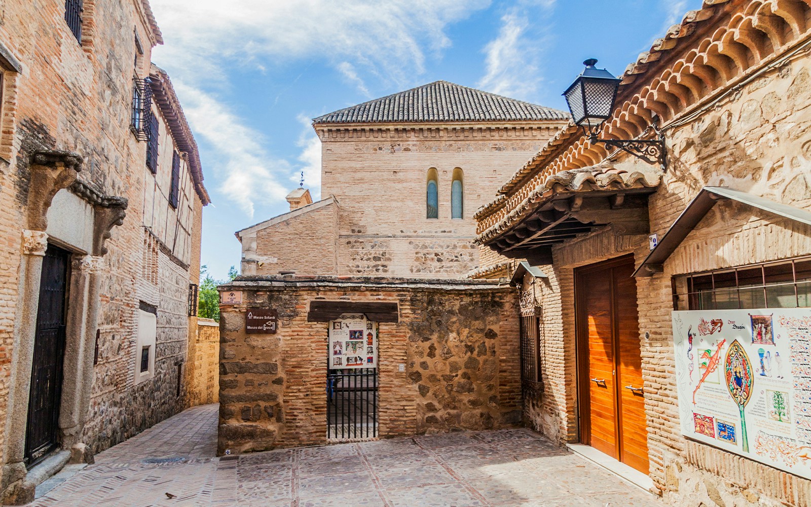 Toledo's Jewish Quarter street with historic stone buildings and a view of the Toledo Cathedral in the background.
