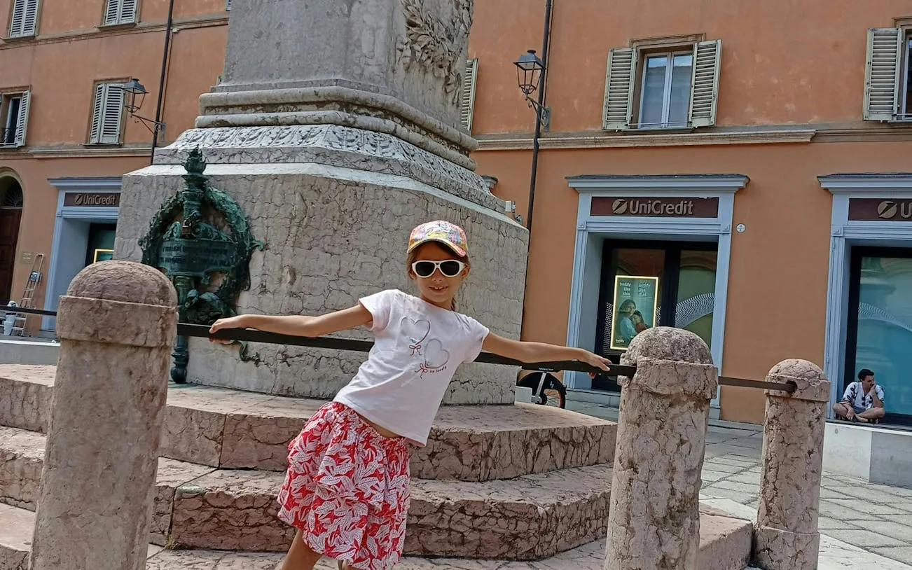 Child posing by a historic monument in Bologna during a self-guided city exploration game.