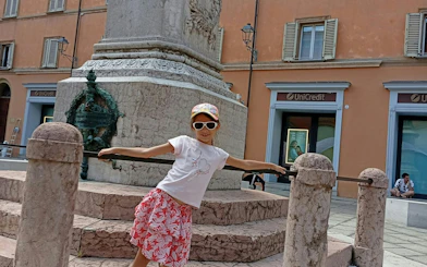 Child posing by a historic monument in Bologna during a self-guided city exploration game.