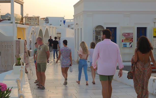 People walking through a white-washed street in Oia, Santorini, near Skiza Pizzeria Cafe.