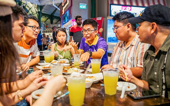 Group enjoying Singapore street food at a night market table.