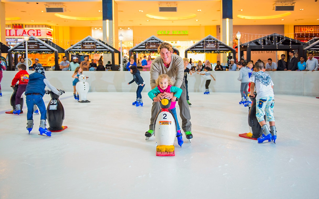 Children and adults ice skating with penguin aids at Dubai Ice Rink.