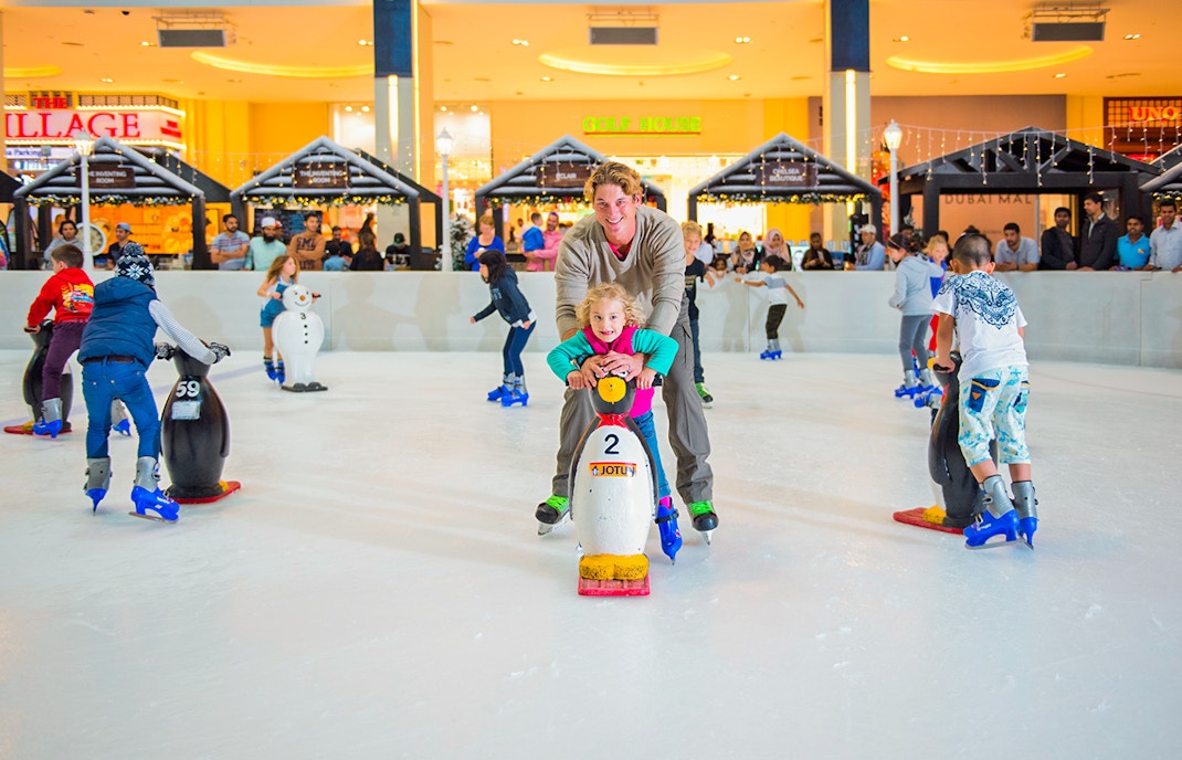 Children and adults ice skating with penguin aids at Dubai Ice Rink.