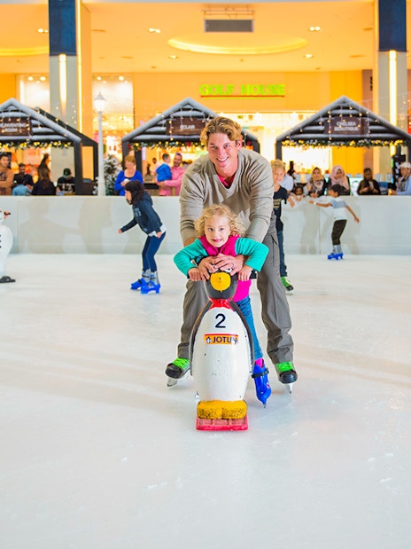 Children and adults ice skating with penguin aids at Dubai Ice Rink.