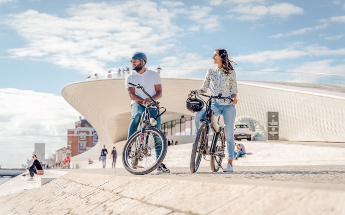 Tourists on ebikes by riverside near modern architecture in Lisbon.