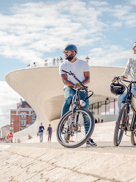 Tourists on ebikes by riverside near modern architecture in Lisbon.