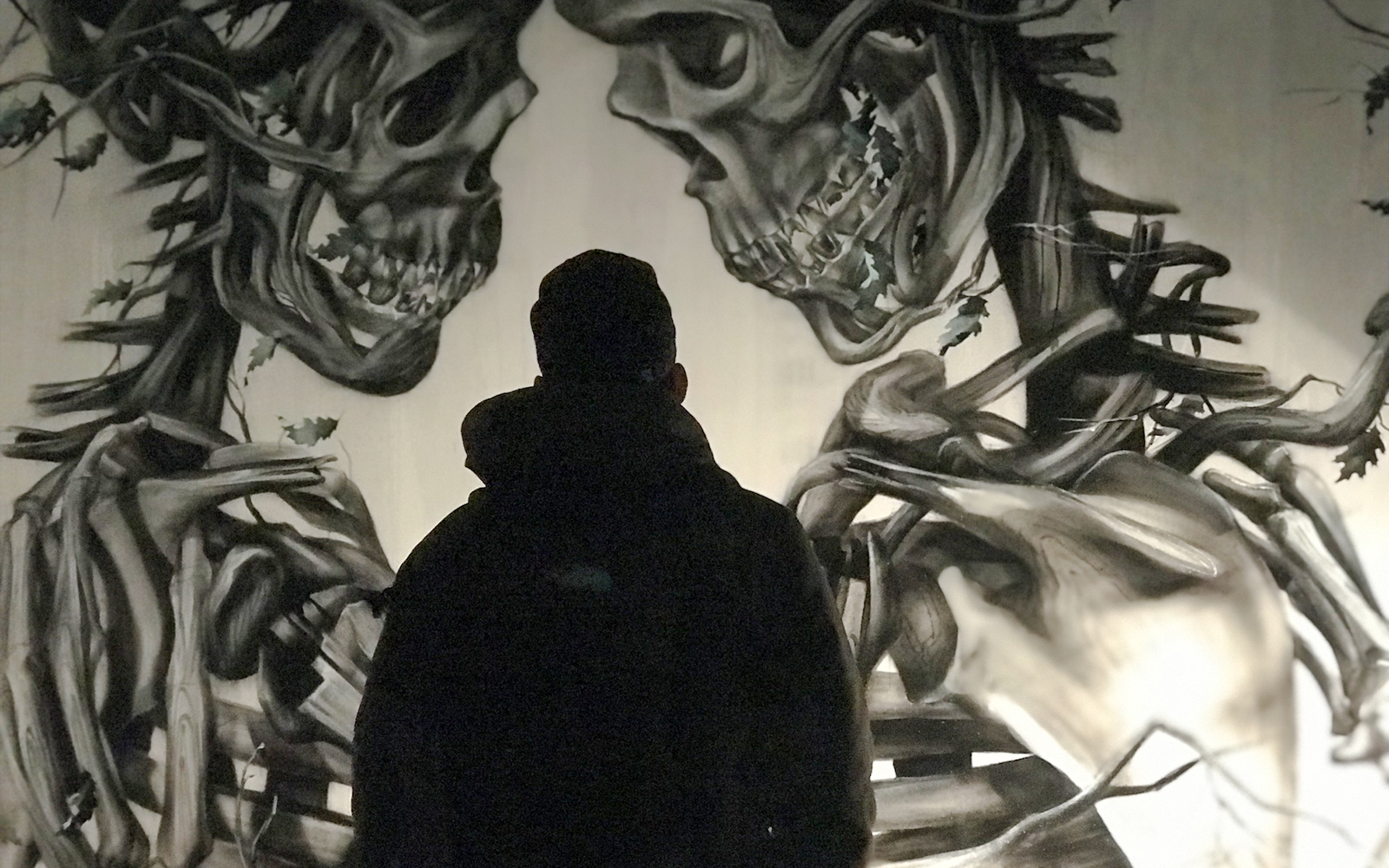 Person viewing mural of intertwined skeletal figures by Vegan Flava, titled A Layer of Soil.