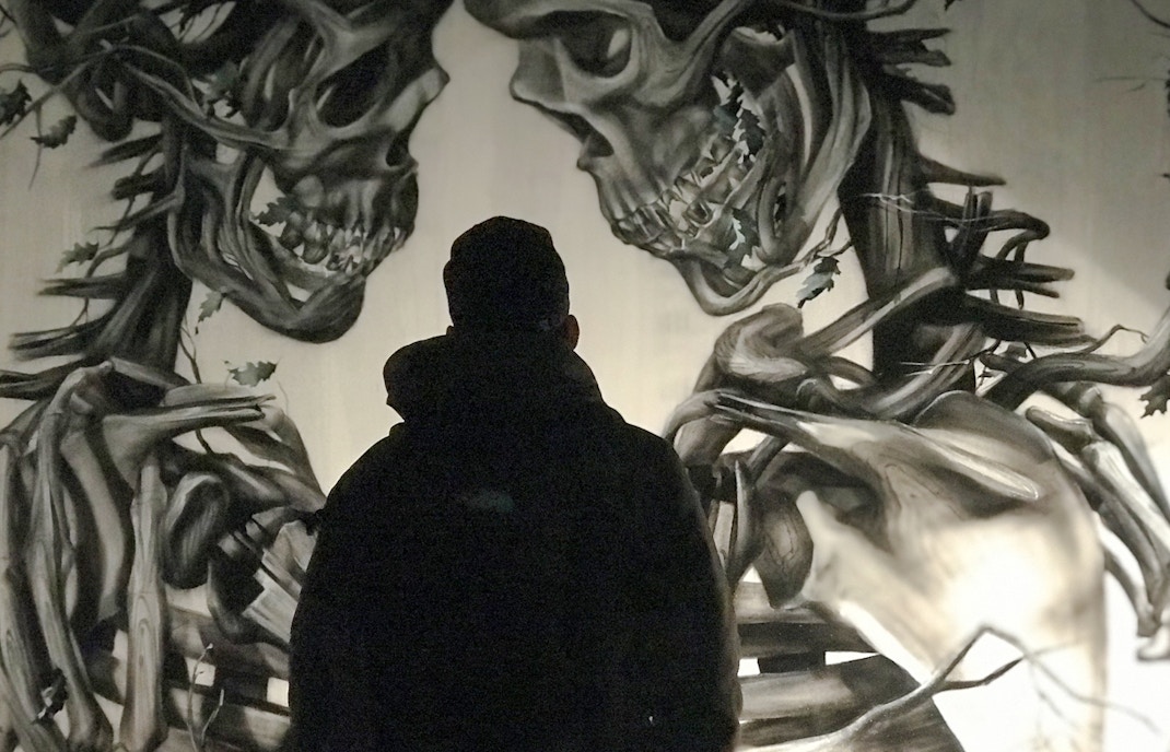 Person viewing mural of intertwined skeletal figures by Vegan Flava, titled A Layer of Soil.