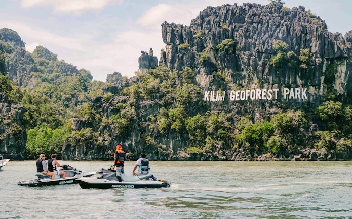 Jet skis near limestone cliffs at Kilim Geoforest Park, Langkawi.