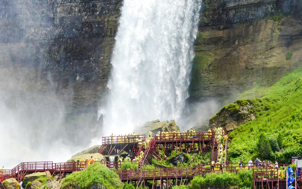 Visitors on wooden walkways near Bridal Veil Falls, Niagara, with mist and lush greenery.