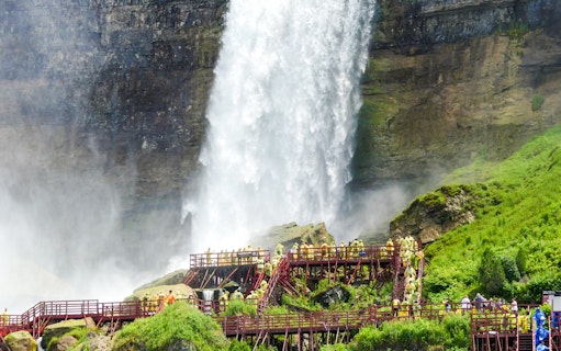 Visitors on wooden walkways near Bridal Veil Falls, Niagara, with mist and lush greenery.
