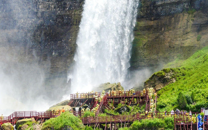 Visitors on wooden walkways near Bridal Veil Falls, Niagara, with mist and lush greenery.