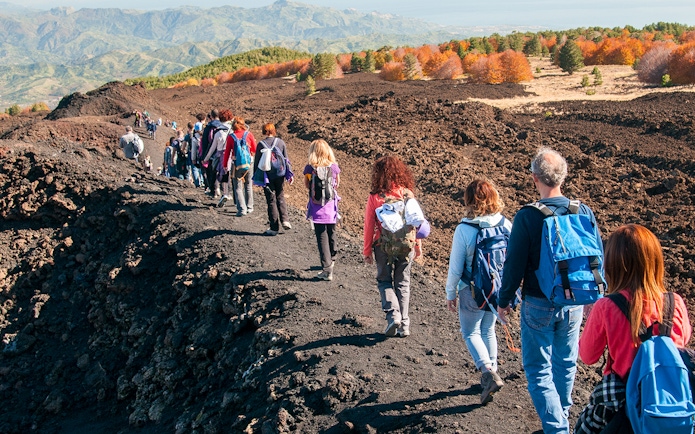 Group hiking on Mount Etna's volcanic terrain during afternoon guided tour.