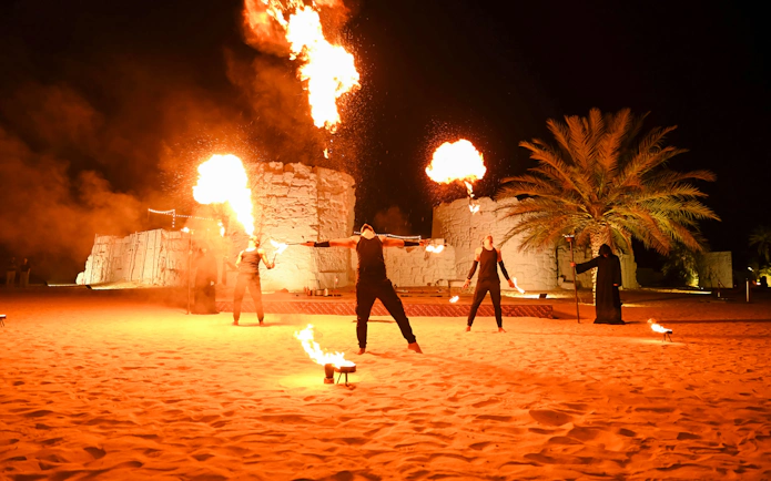 Fire performers at Dubai desert safari with flames against night sky.