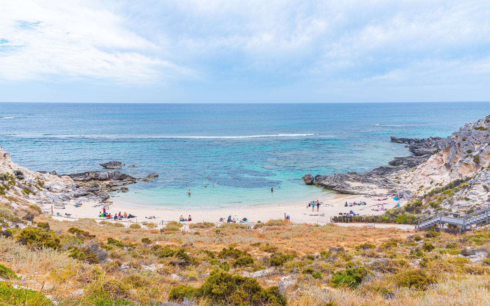 Beachgoers at a scenic cove with rocky cliffs and turquoise water in Rottnest Island, Australia.