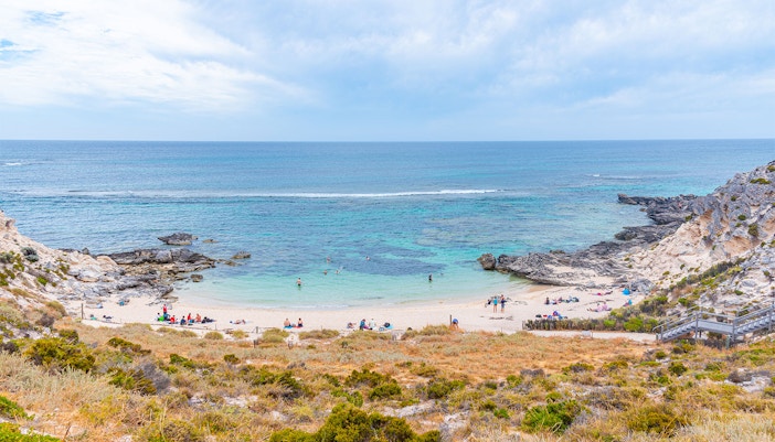Beachgoers at a scenic cove with rocky cliffs and turquoise water in Rottnest Island, Australia.
